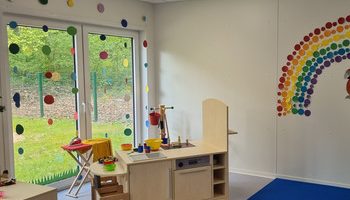 Ein helles Klassenzimmer im PARI Kinderhaus mit einem Spielküchen-Set, einem blauen Teppich.