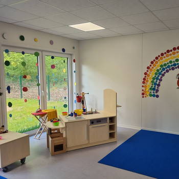 Ein helles Klassenzimmer im PARI Kinderhaus mit einem Spielküchen-Set, einem blauen Teppich.