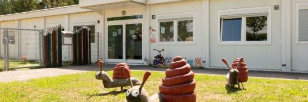 Drei große, bunte Schneckenskulpturen mit roten Häusern zieren das Gras vor einer Kindertageseinrichtung.