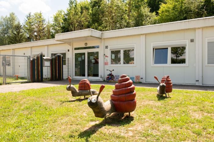 Drei große, bunte Schneckenskulpturen mit roten Häusern zieren das Gras vor einer Kindertageseinrichtung.